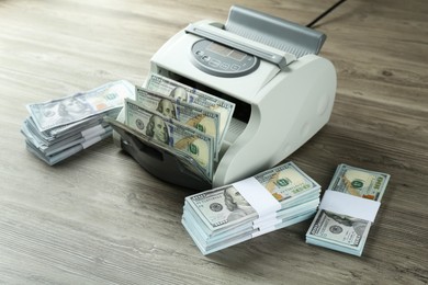 Photo of Money counter machine with dollar banknotes on wooden table