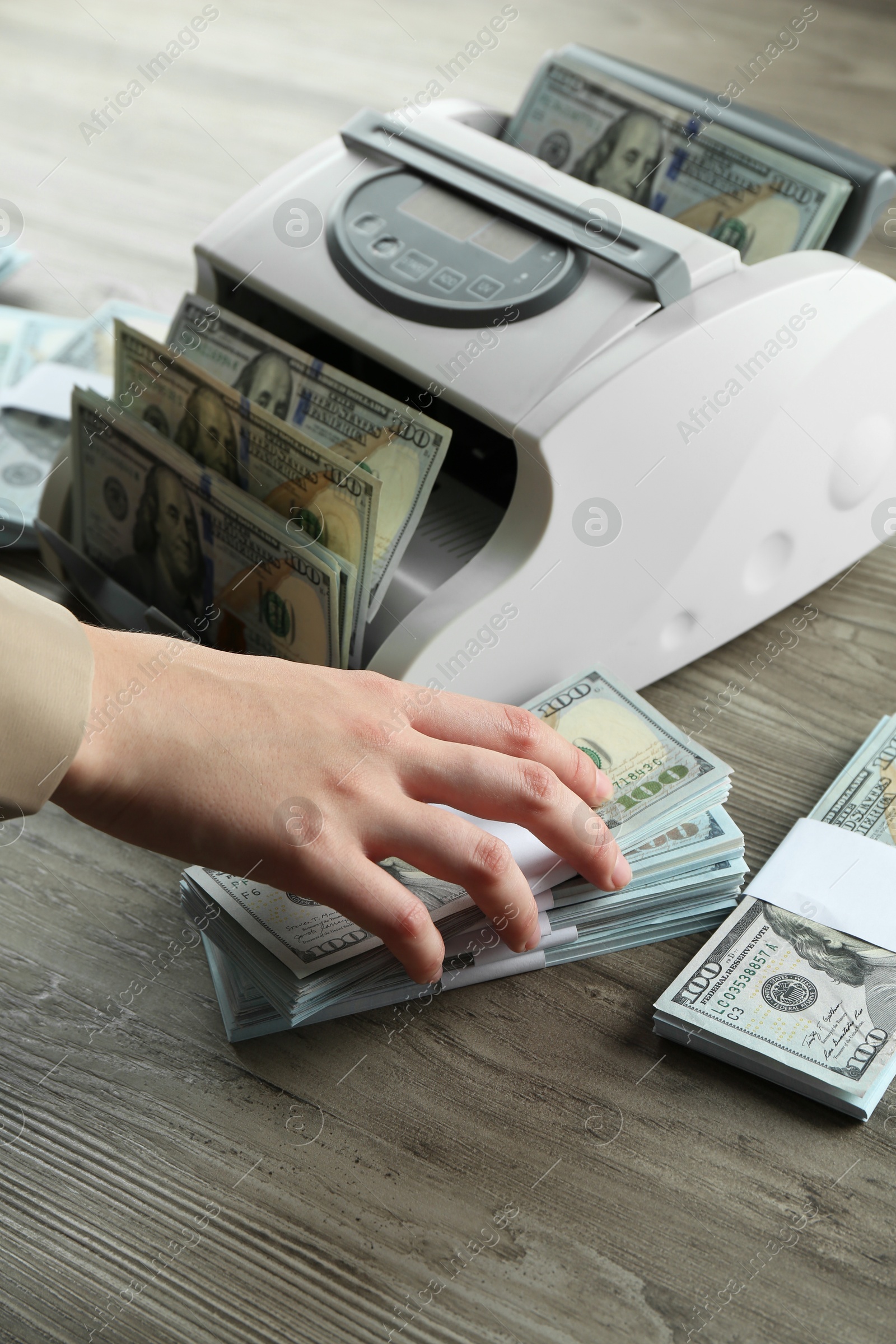 Photo of Woman using money counter machine at wooden table, closeup