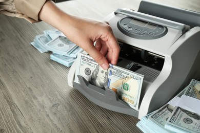 Woman using money counter machine at wooden table, closeup