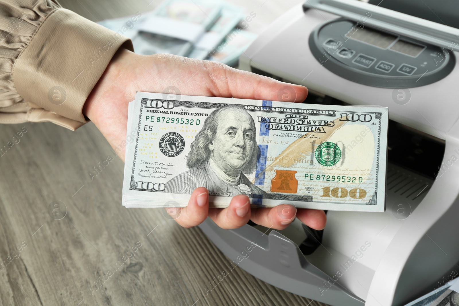 Photo of Woman with dollar banknotes near money counter machine at wooden table, closeup