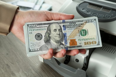 Photo of Woman with dollar banknotes near money counter machine at wooden table, closeup