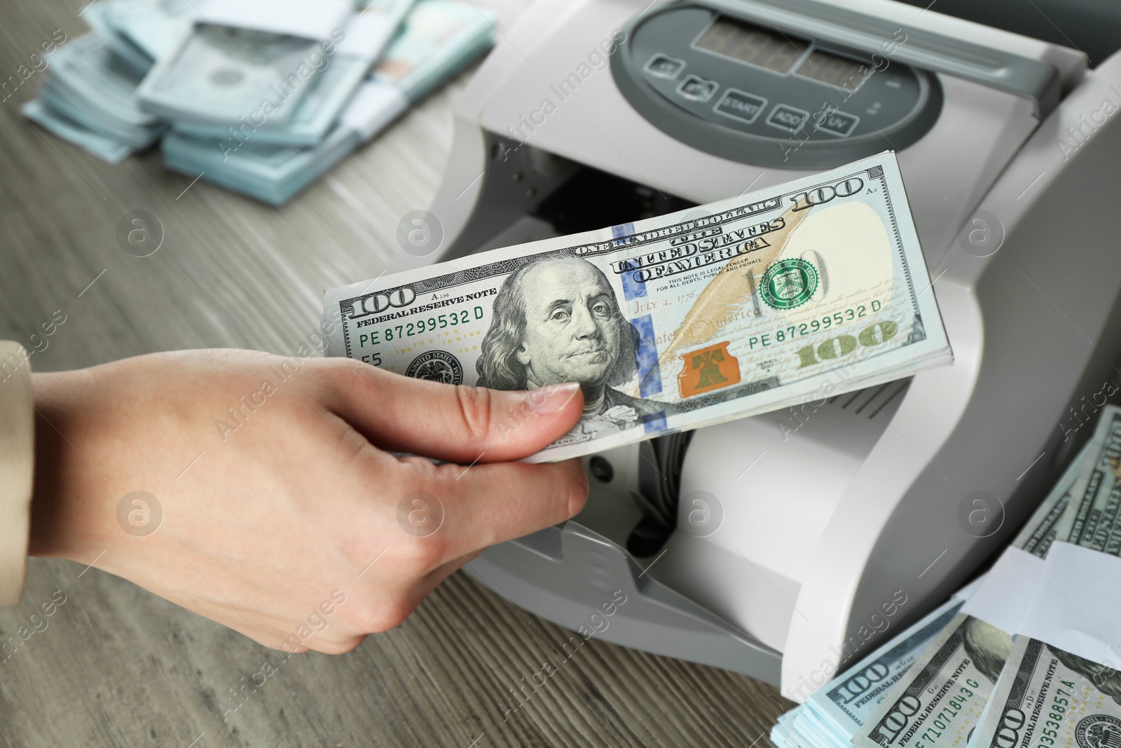 Photo of Woman using money counter machine at wooden table, closeup