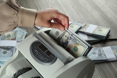 Photo of Woman using money counter machine at wooden table, closeup