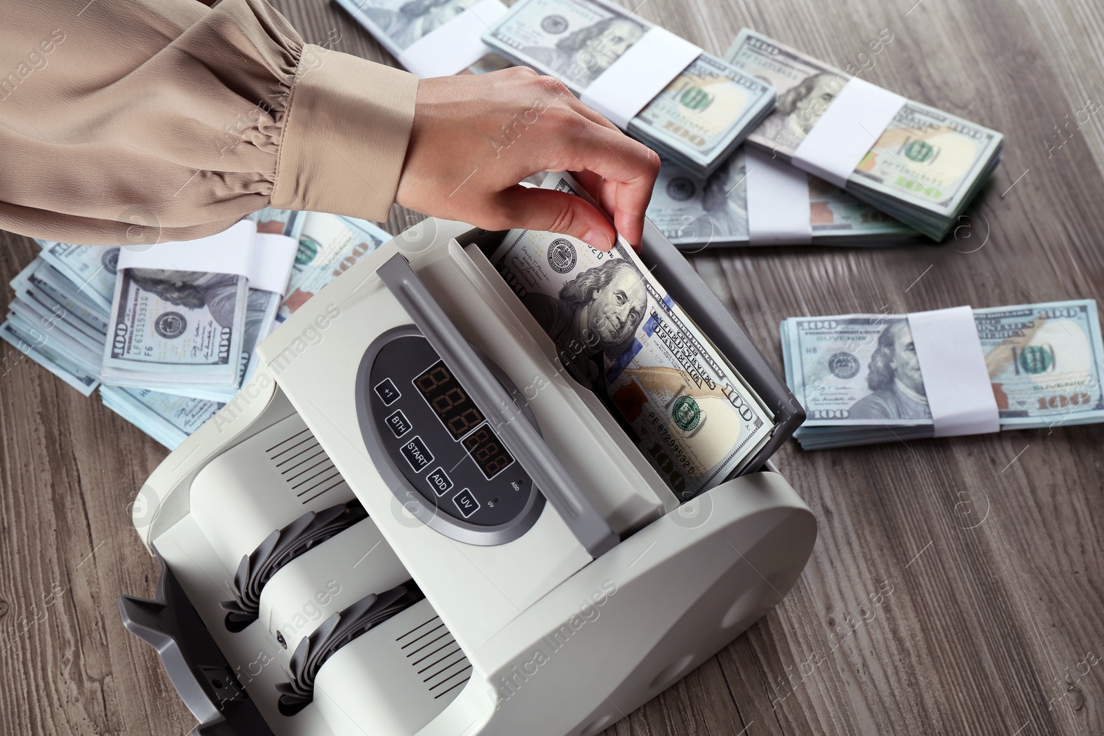 Photo of Woman using money counter machine at wooden table, closeup