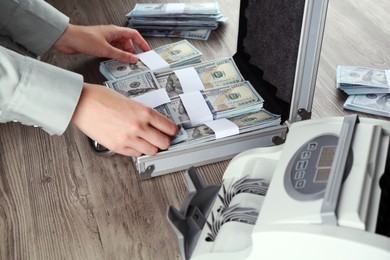 Photo of Woman counting dollar banknotes at wooden table, closeup