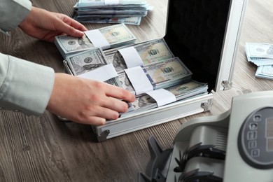 Photo of Woman counting dollar banknotes at wooden table, closeup