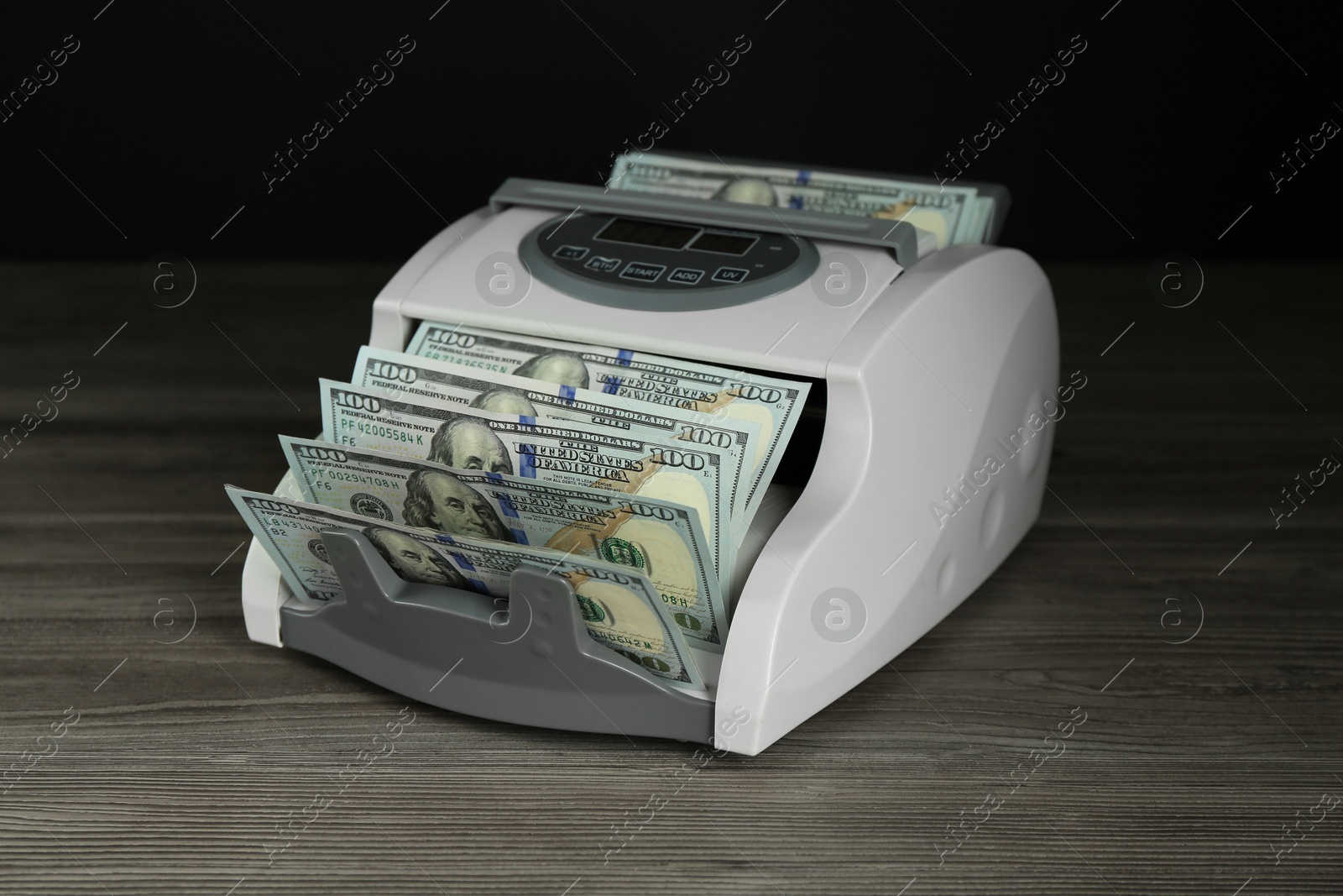 Photo of Money counter machine with dollar banknotes on wooden table