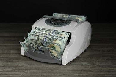 Photo of Money counter machine with dollar banknotes on wooden table