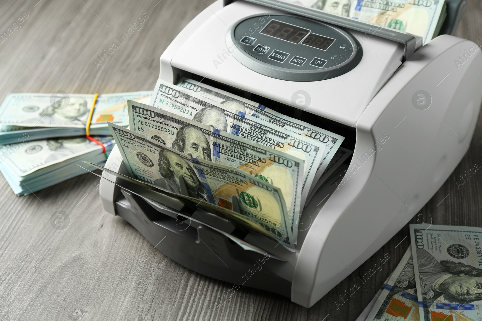 Photo of Money counter machine with dollar banknotes on wooden table