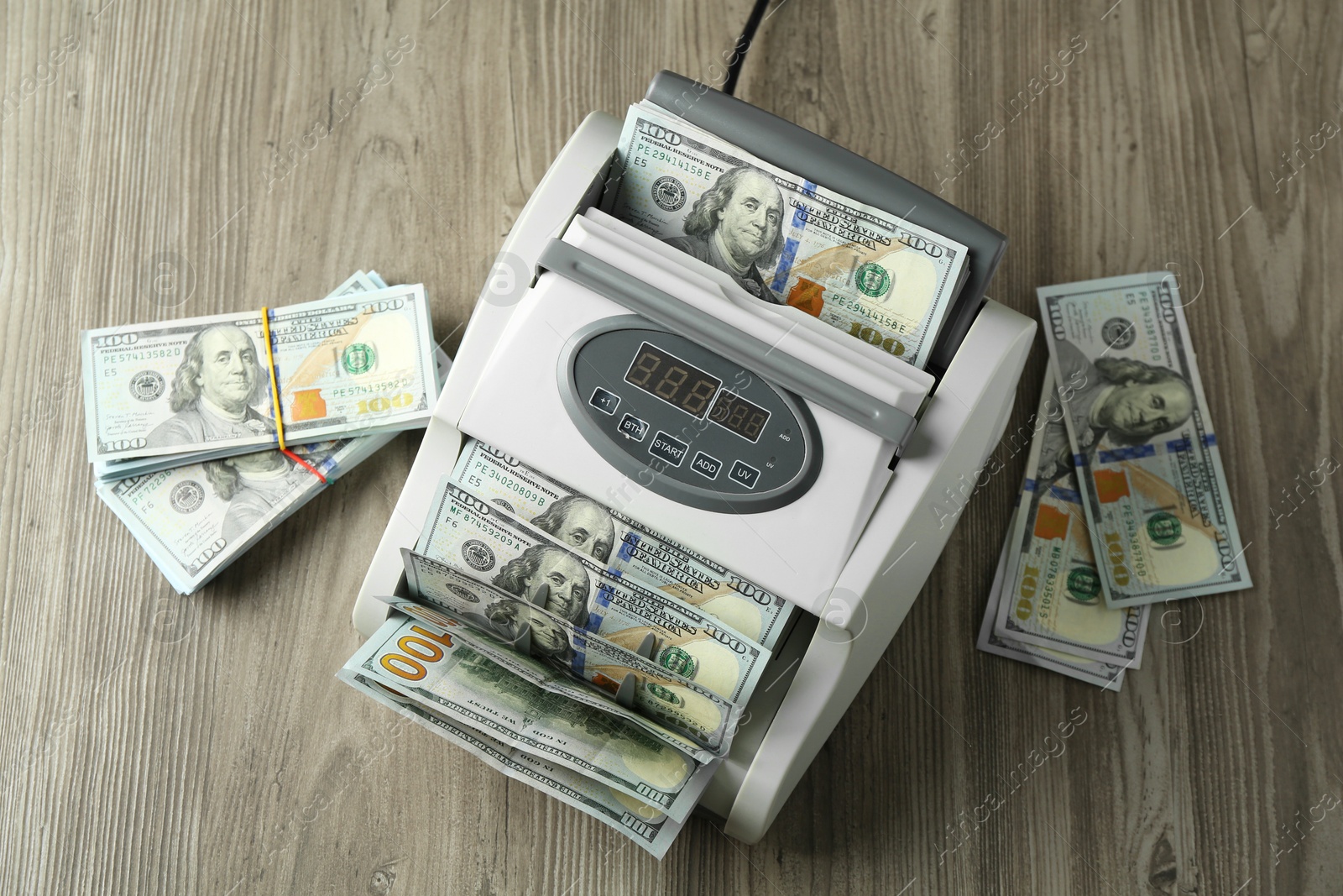 Photo of Money counter machine with dollar banknotes on wooden table, above view