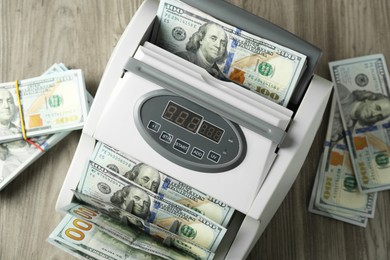 Photo of Money counter machine with dollar banknotes on wooden table, above view