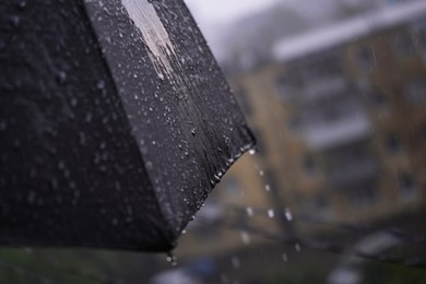 Photo of Open black umbrella outdoors on rainy day, closeup. Space for text