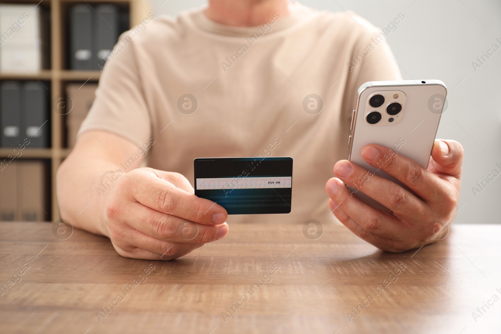 Photo of Man with credit card and smartphone at wooden table indoors, closeup