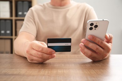 Photo of Man with credit card and smartphone at wooden table indoors, closeup