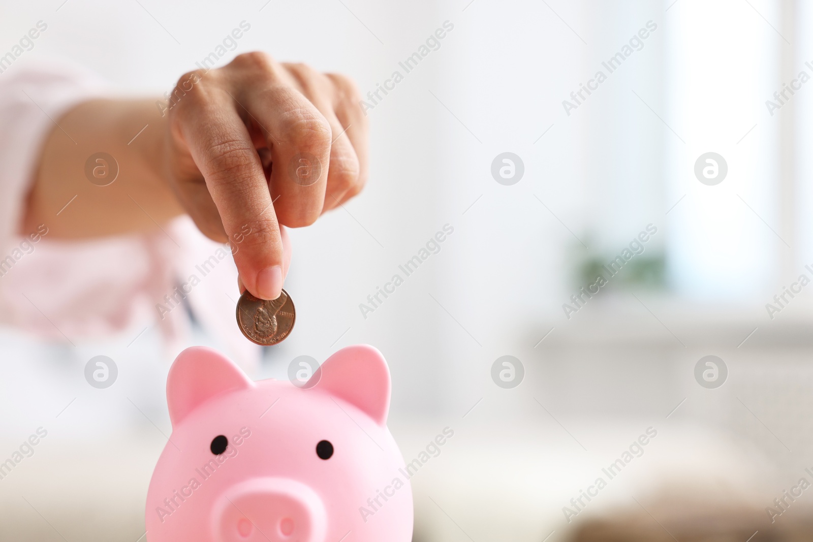 Photo of Woman putting coin into pink piggy bank at home, closeup. Space for text