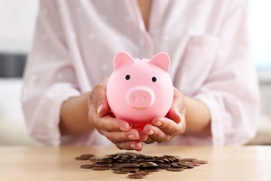 Photo of Woman with piggy bank and money at table indoors, closeup