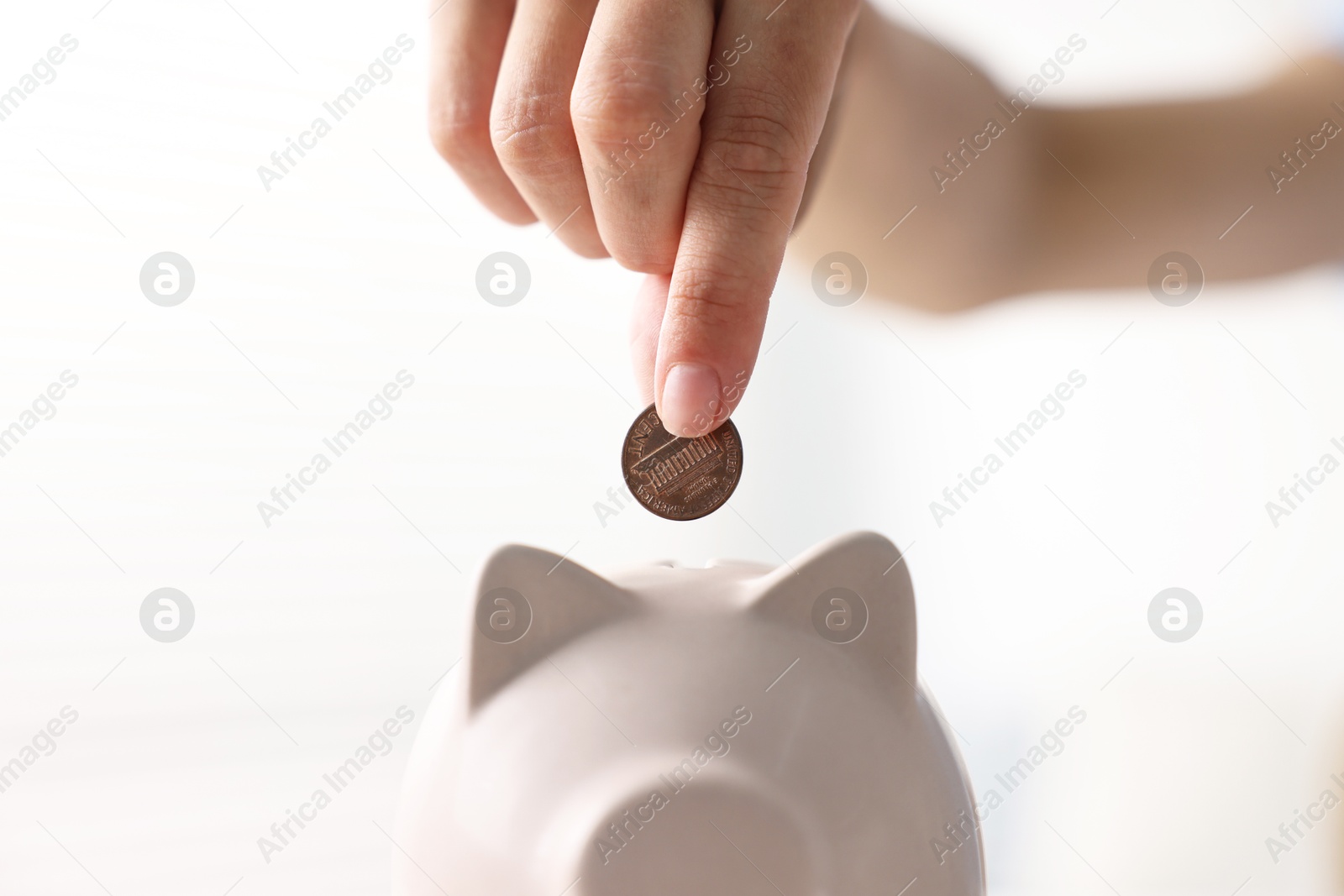 Photo of Woman putting coin into piggy bank indoors, closeup