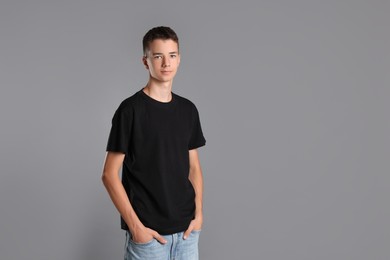 Teenage boy wearing black t-shirt on grey background, space for text