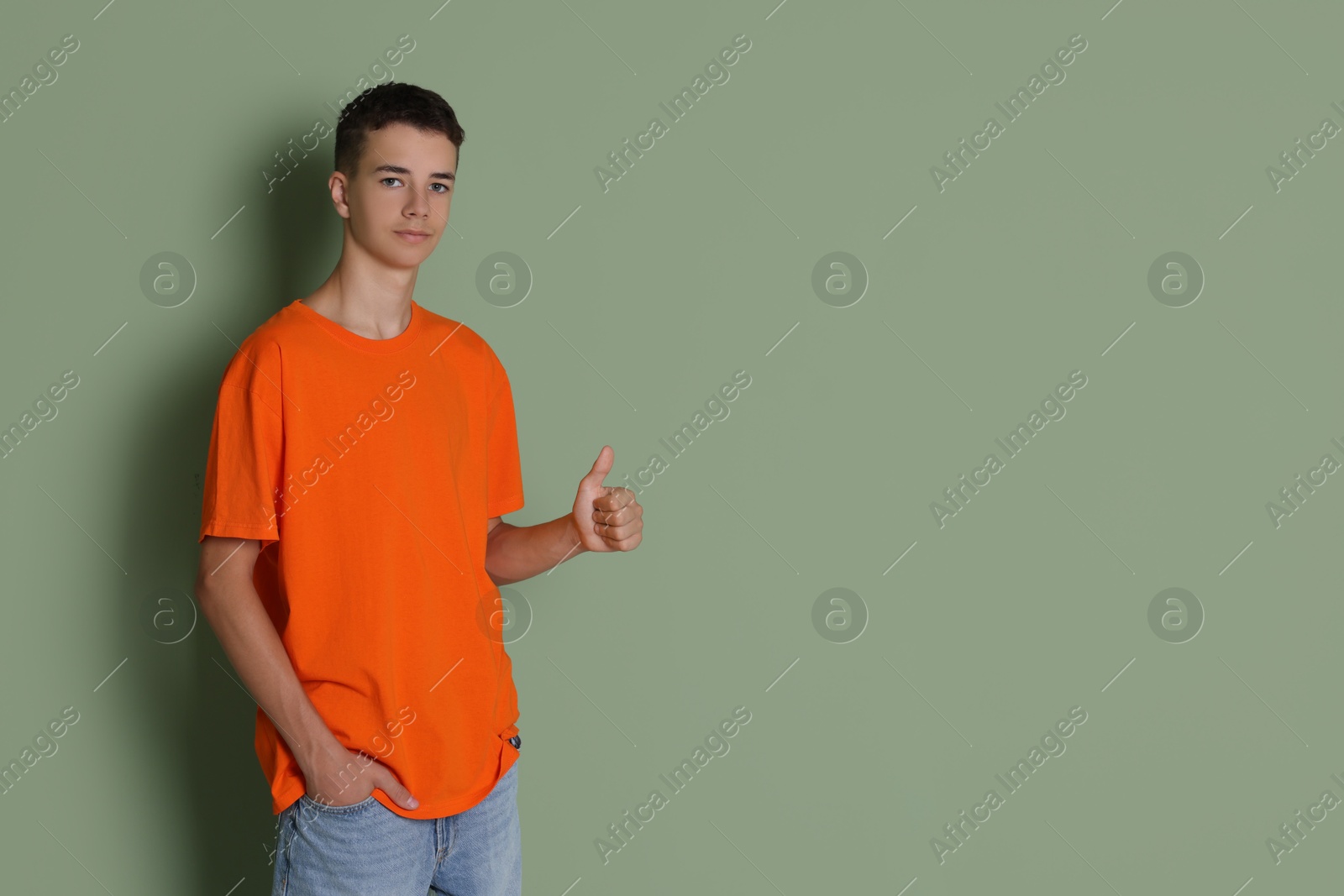 Photo of Teenage boy wearing orange t-shirt and showing thumbs up on green background, space for text