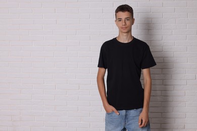 Teenage boy wearing black t-shirt near white brick wall, space for text