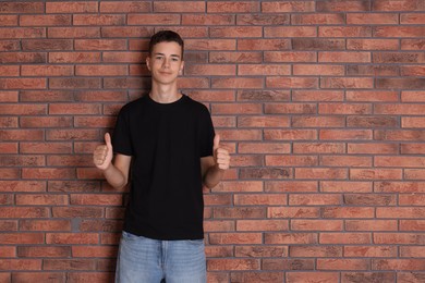 Teenage boy wearing black t-shirt and showing thumbs up near brick wall