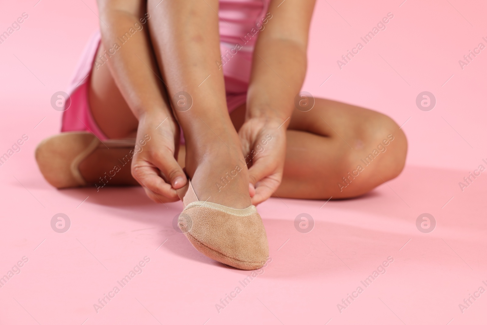 Photo of Little ballerina putting on pointe shoes against pink background, closeup