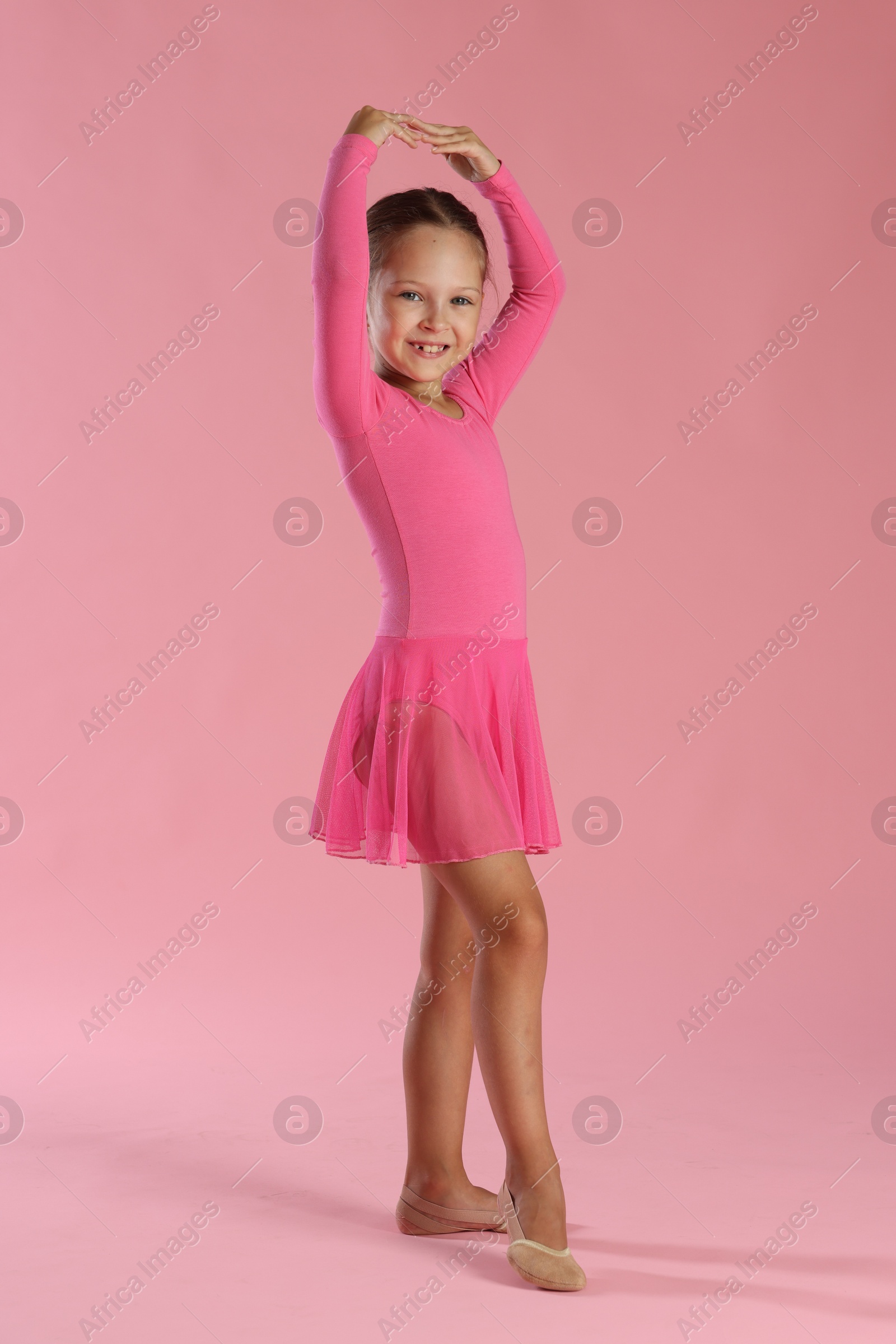 Photo of Little ballerina practicing dance moves on pink background