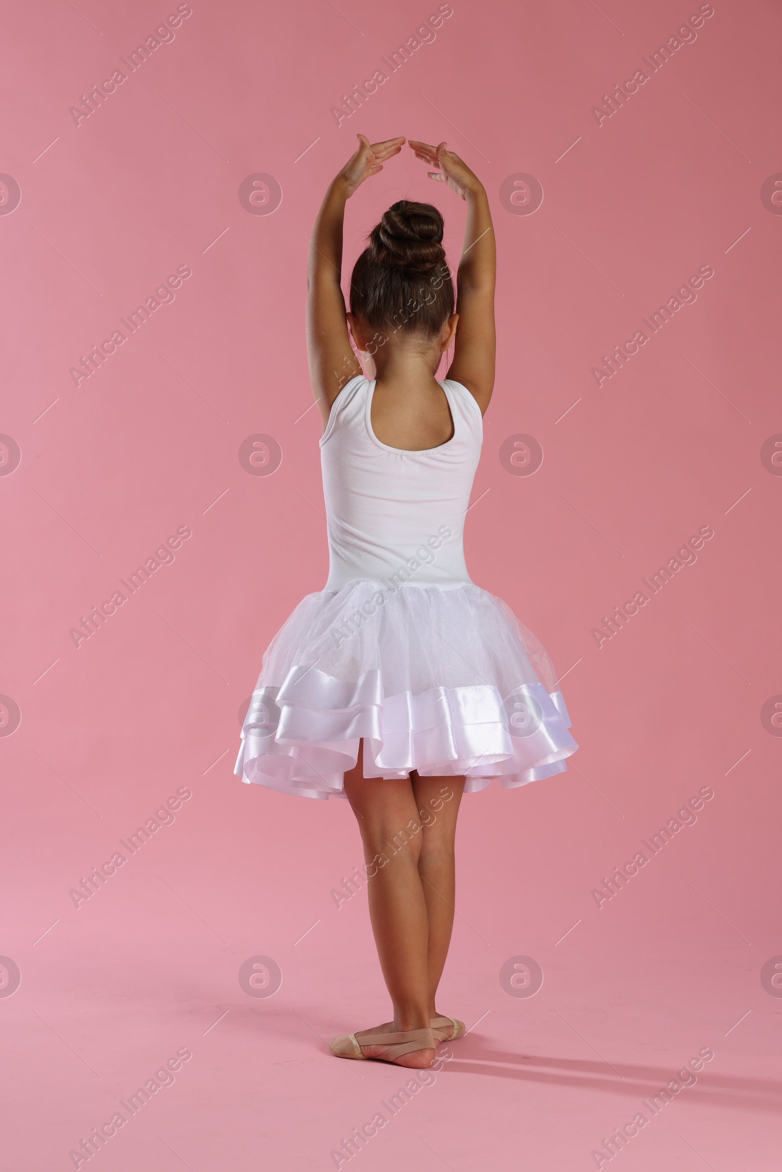 Photo of Little ballerina practicing dance moves on pink background, back view