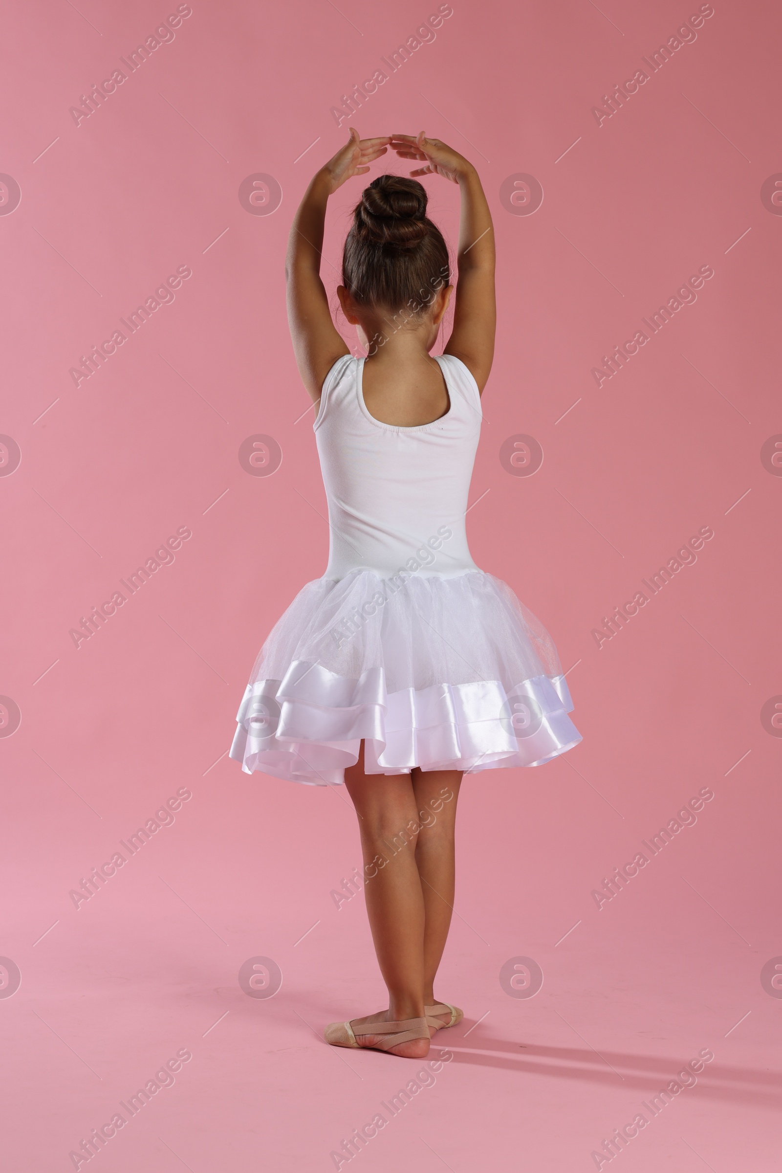 Photo of Little ballerina practicing dance moves on pink background, back view