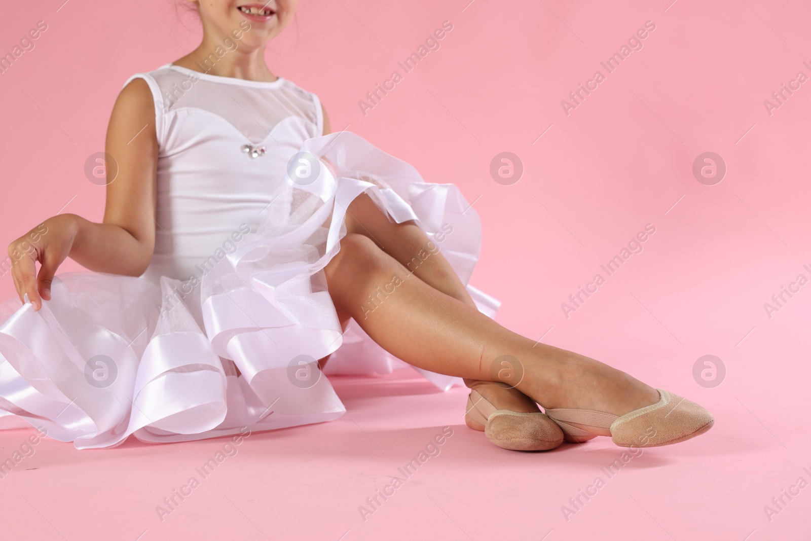 Photo of Little ballerina wearing pointe shoes on pink background, closeup