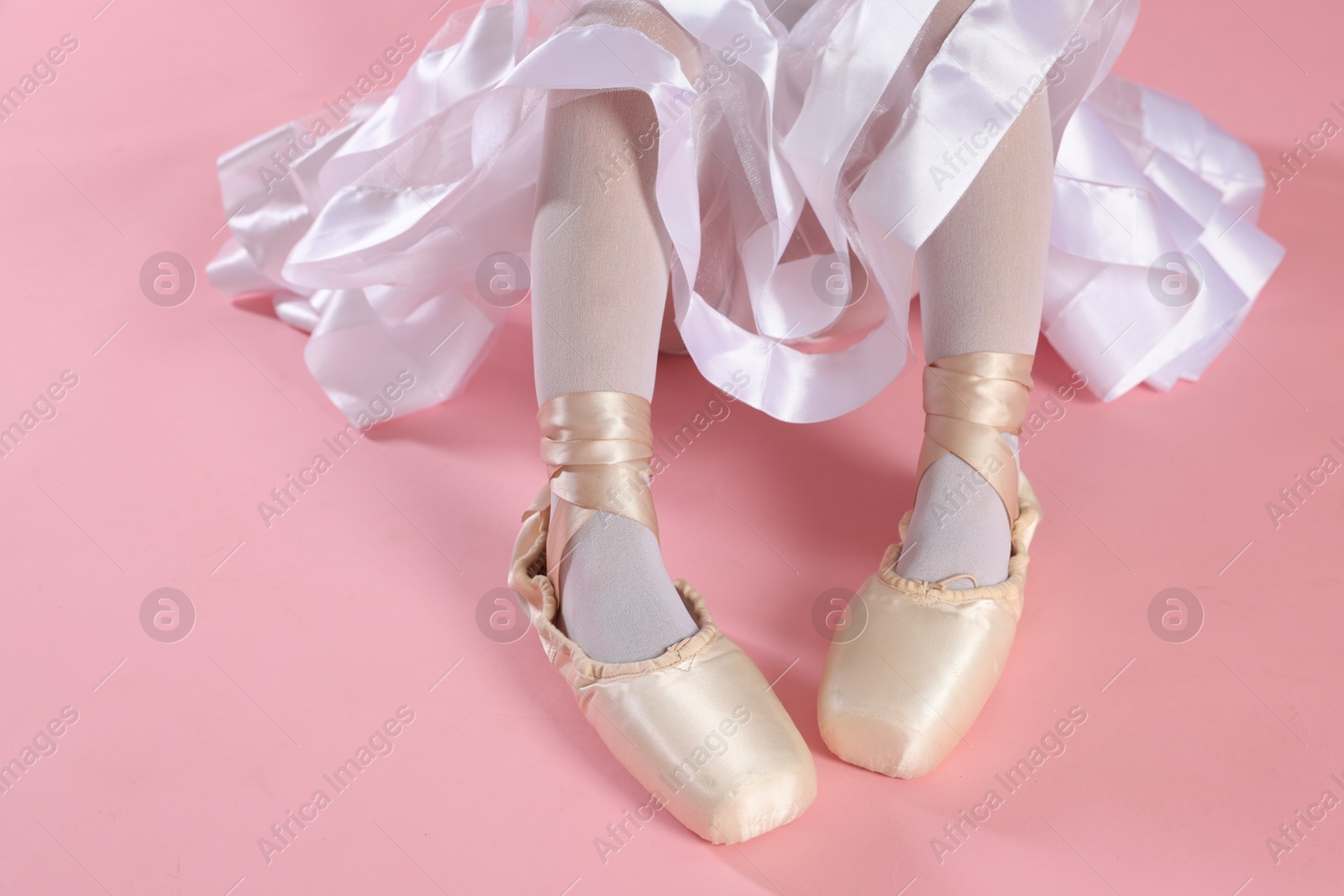 Photo of Little ballerina wearing pointe shoes on pink background, closeup