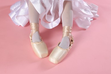 Little ballerina wearing pointe shoes on pink background, closeup