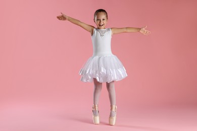 Photo of Little ballerina practicing dance moves on pink background