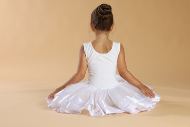 Photo of Little ballerina on beige background, back view