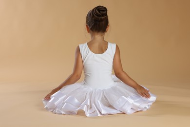 Photo of Little ballerina on beige background, back view