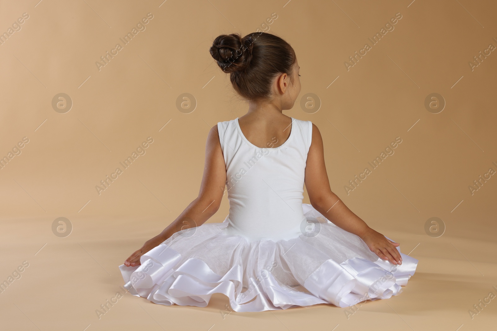 Photo of Little ballerina on beige background, back view