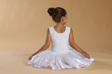 Photo of Little ballerina on beige background, back view