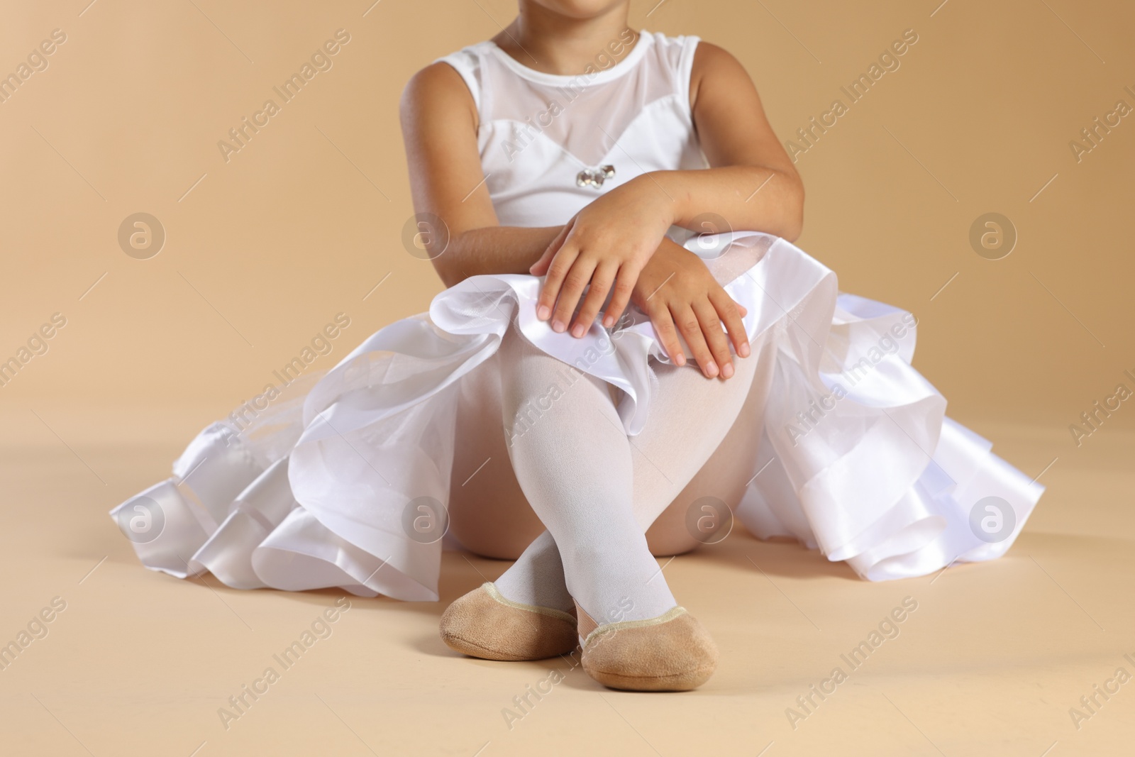 Photo of Little ballerina wearing pointe shoes on beige background, closeup