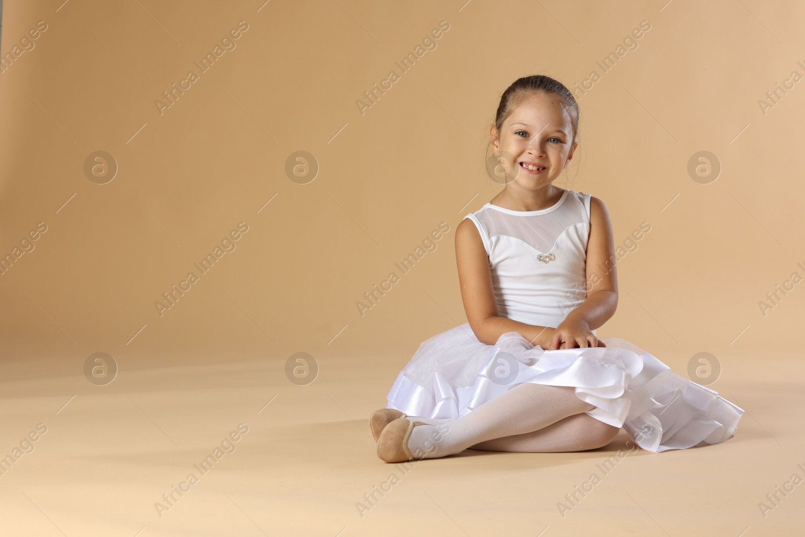 Photo of Portrait of little ballerina on beige background, space for text