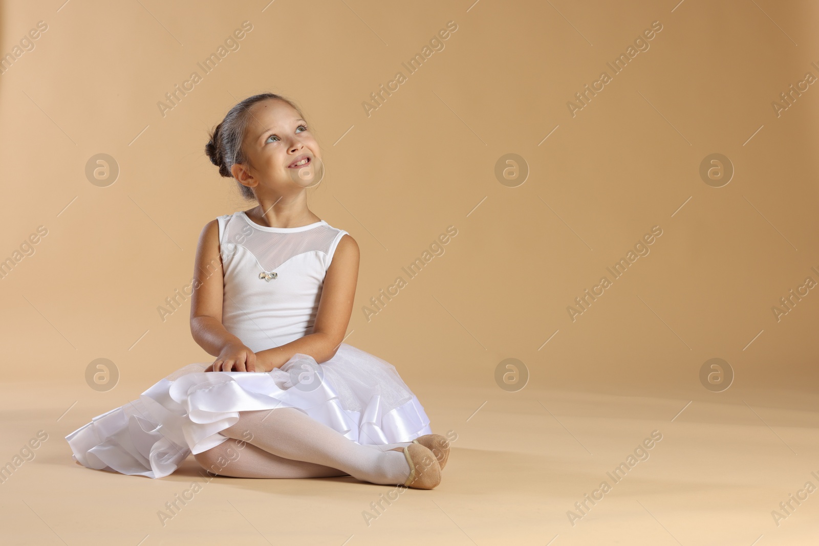 Photo of Portrait of little ballerina on beige background, space for text