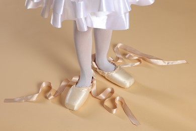 Photo of Little ballerina wearing pointe shoes on beige background, closeup