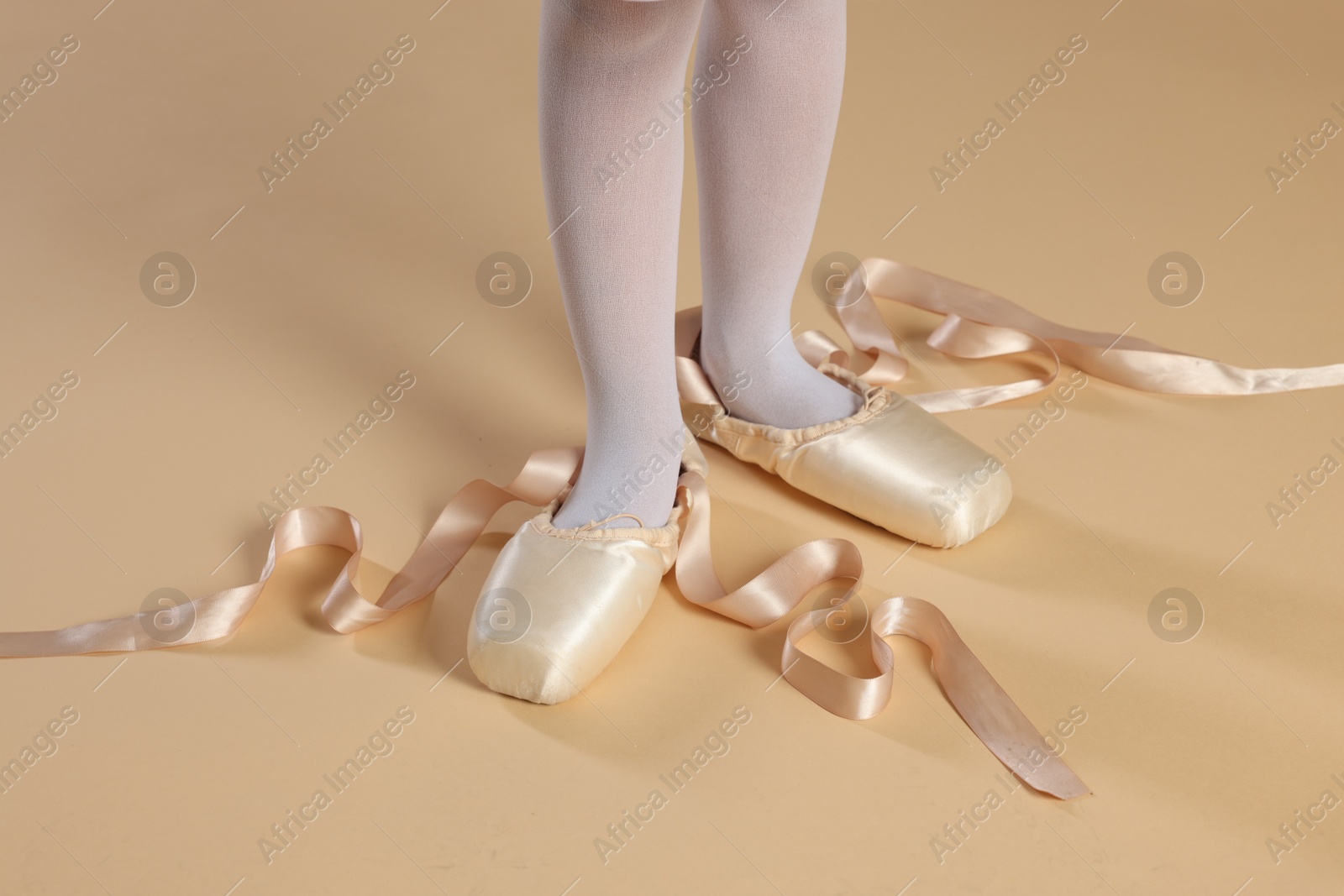 Photo of Little ballerina wearing pointe shoes on beige background, closeup