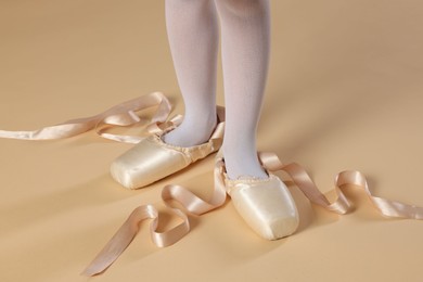 Photo of Little ballerina wearing pointe shoes on beige background, closeup