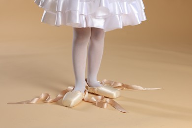 Little ballerina wearing pointe shoes on beige background, closeup