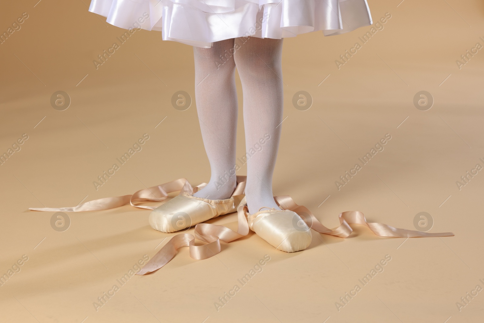 Photo of Little ballerina wearing pointe shoes on beige background, closeup