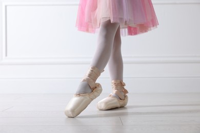 Little ballerina practicing dance moves near white wall indoors, closeup