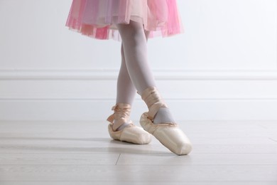 Photo of Little ballerina practicing dance moves near white wall indoors, closeup