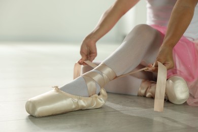 Photo of Little ballerina tying pointe shoes indoors, closeup