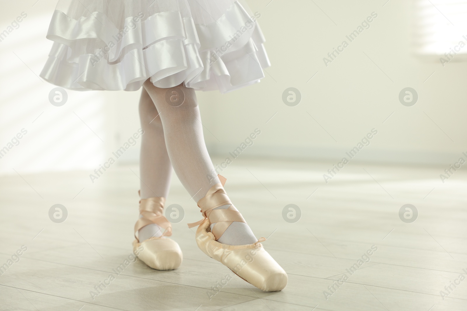 Photo of Little ballerina practicing dance moves indoors, closeup. Space for text