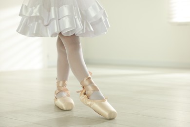 Photo of Little ballerina practicing dance moves indoors, closeup. Space for text